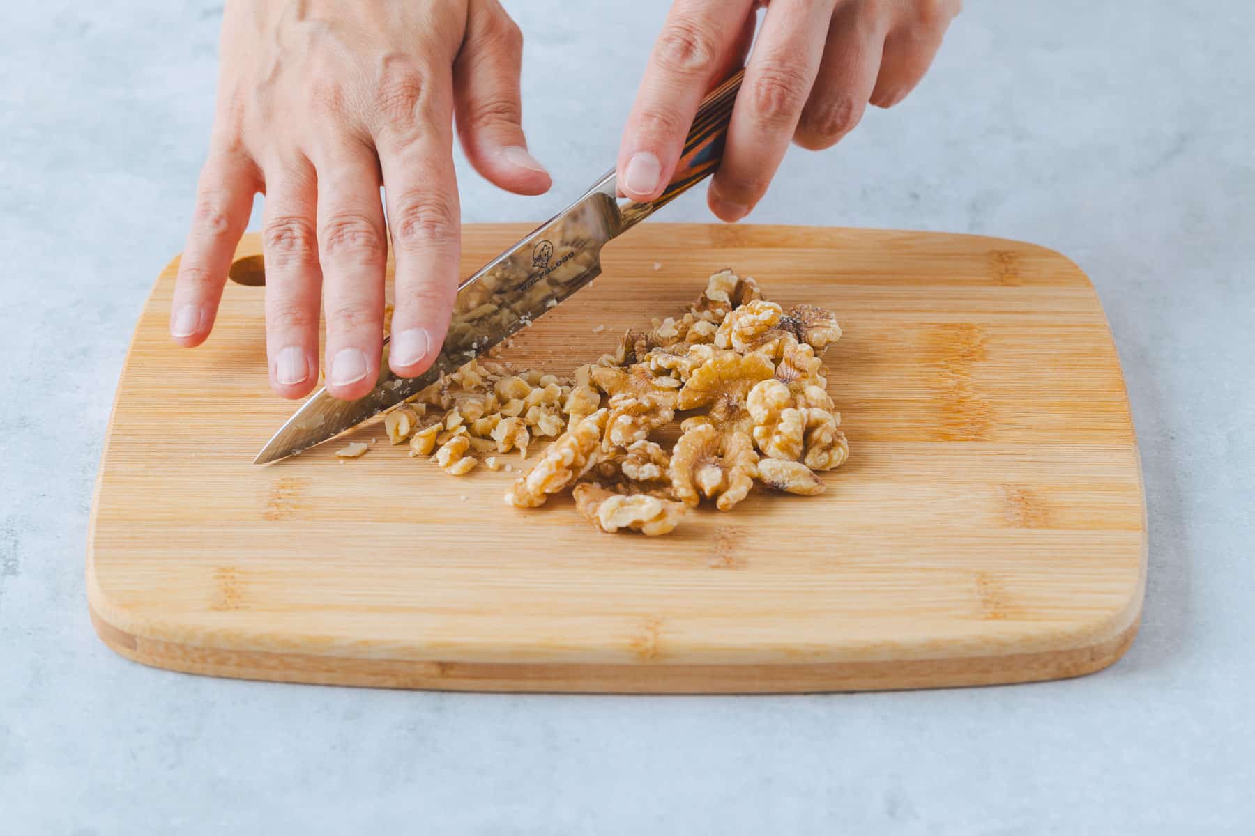 Walnüsse für Bananenbrot werden auf einem Holzbrett mit einem Messer klein gehackt.