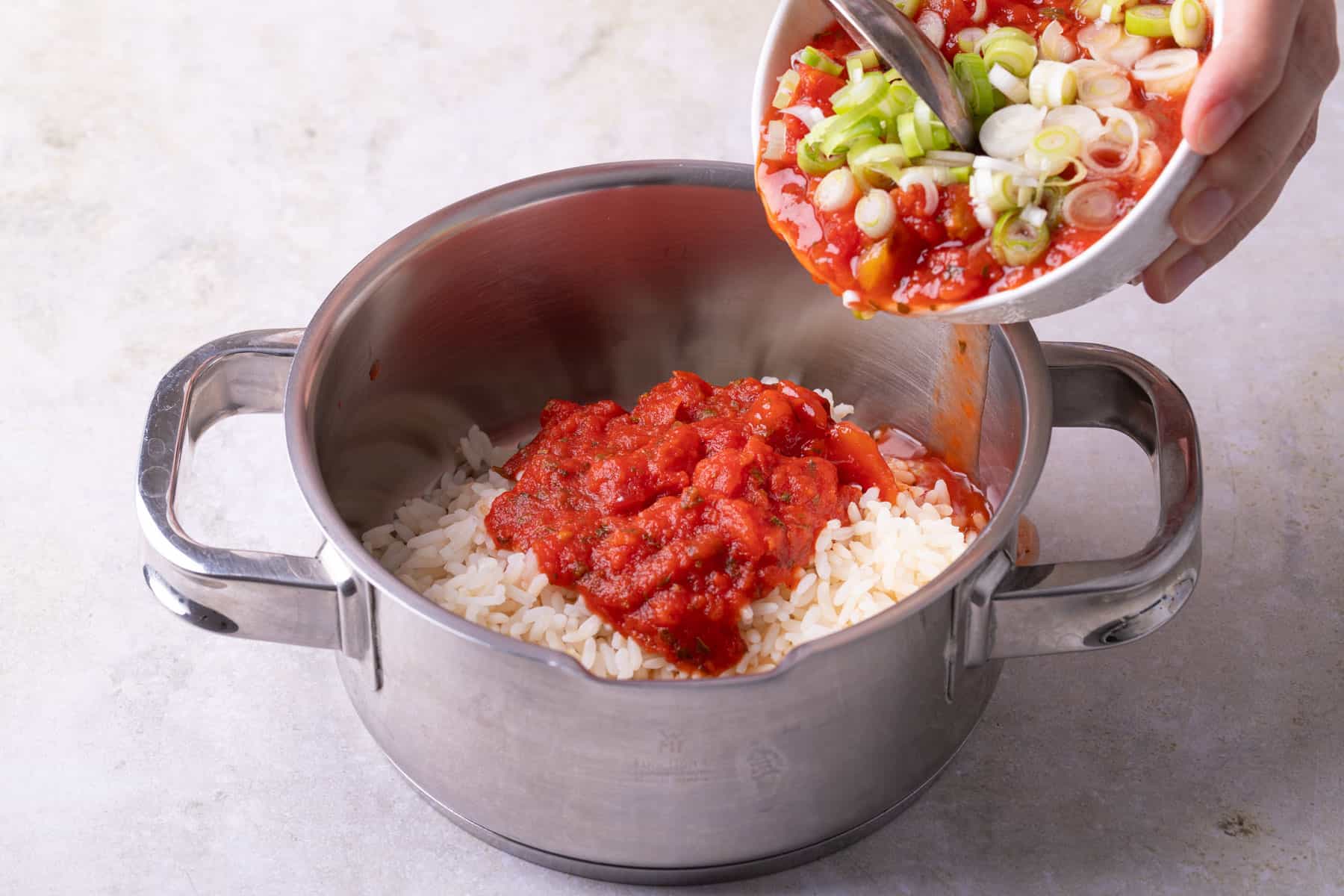 Tomatensoße und Frühlingszwiebeln werden in einen Topf zum Reis gegeben.