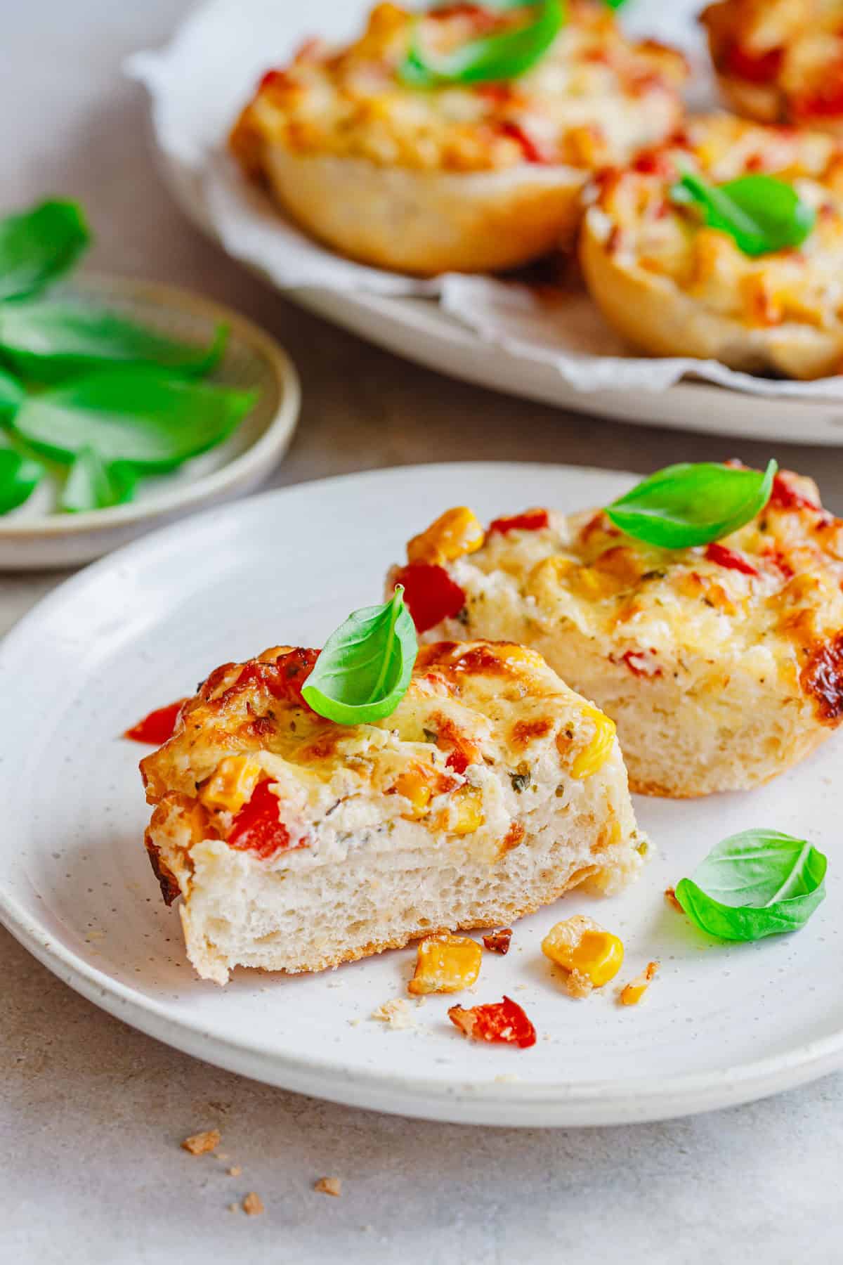 vegetarische Pizzabrötchen mit Schmand aufgeschnitten auf einem Teller mit Basilikum.